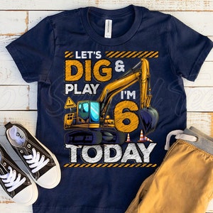 May include: Navy blue t-shirt with a yellow and orange graphic of an excavator and the text "Let's Dig & Play I'm 6 Today". Black canvas sneakers with white laces and a pair of tan sweatpants are next to the shirt.