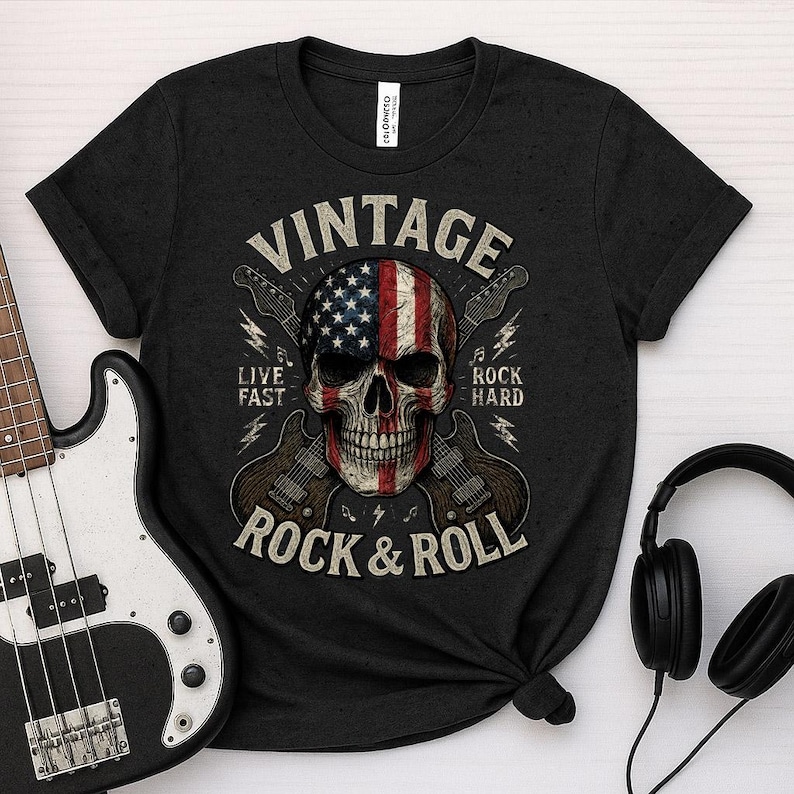 Peut inclure: T-shirt noir avec un motif de cr&acirc;ne orn&eacute; du drapeau am&eacute;ricain, de guitares et les mots "VINTAGE ROCK & ROLL". Le t-shirt porte &eacute;galement les phrases "LIVE FAST" et "ROCK HARD". Une guitare basse et un casque sont dans l'image.