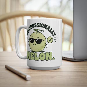 Op de afbeelding: Een witte keramische mok met een cartoonillustratie van een lichtgroene meloen met een zwarte zonnebril. De tekst erboven luidt "PROFESSIONALLY" en eronder "MELON." met een klein groen vinkje naast het meloenkarakter.
