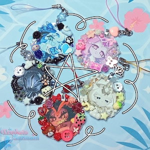 May include: A collection of five circular charms with various designs. Each charm features a central image surrounded by decorative elements like beads, flowers, and small figurines. The charms have attached lanyards for hanging.