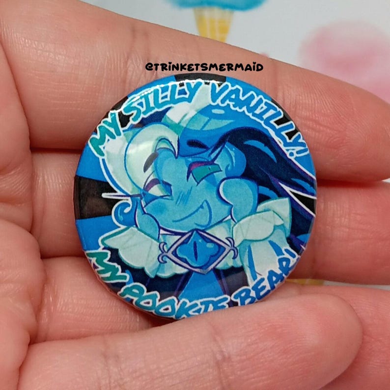 May include: A blue and white button with a cartoon illustration of two characters. The text on the button reads "My Silly Vanilla Rookie Bear!"