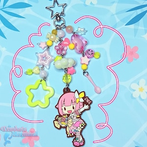 May include: A whimsical keychain featuring a star-shaped clasp and a collection of colorful charms. The charms include stars, flowers, hearts, and a cartoon character. The color palette is predominantly pink, yellow, and green, with a touch of clear beads.