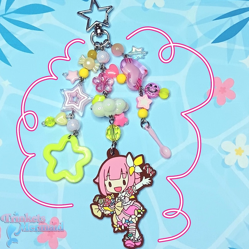 May include: A whimsical keychain featuring a star-shaped clasp and a collection of colorful charms. The charms include stars, flowers, hearts, and a cartoon character. The color palette is predominantly pink, yellow, and green, with a touch of clear beads.