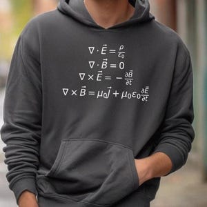 以下が含まれることがあります： 白文字で4つの物理方程式が書かれた濃いグレーのパーカー。∇ · E = ρ/ε₀、∇ · B = 0、∇ × E = -∂B/∂t、∇ × B = μ₀J + μ₀ε₀∂E/∂t。