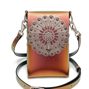 Puede incluir: Un pequeño bolso bandolera de cuero naranja y verde iridiscente con un diseño floral plateado en la parte delantera. El bolso tiene una correa negra ajustable.