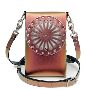 Może przedstawiać: Mała, tęczowa, czerwona skórzana torebka na ramię z okrągłym srebrnym wzorem, który zawiera biały, geometryczny wzór. Torebka ma długi, regulowany pasek.