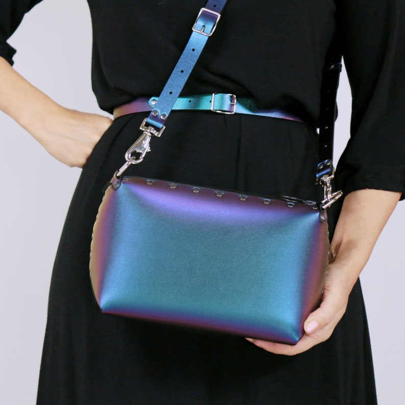 May include: Iridescent crossbody bag with matching belt and strap. The bag is a rectangular shape with a zipper closure and silver-tone rivets along the top edge. The strap and belt have silver-tone buckles.