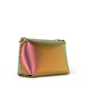 May include: A small iridescent handbag with a gold-toned zipper and a gold-toned ring on the strap. The bag is made of a smooth, shiny material and has a rectangular shape.