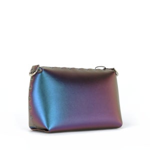May include: A small, iridescent clutch bag with a rectangular shape. The bag transitions from blue to purple hues and features silver-toned rivets along the side and a silver ring for a strap. The top edge has decorative stitching.