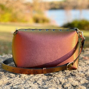 May include: A iridescent, multi-coloured, leather shoulder bag with a gold buckle and a long strap. The bag has a rounded shape and is decorated with small metal studs.