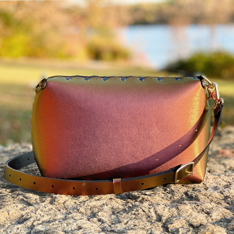 May include: A iridescent, multi-coloured, leather shoulder bag with a gold buckle and a long strap. The bag has a rounded shape and is decorated with small metal studs.