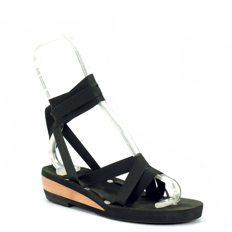 3/4 front view of low wedge ribbon sandal.  Laced with a black ribbon, tied from front to back and around the ankle.  Photo highlights the supportive footbed, composed of 1/4" pad and luxury vegan suede.  Each pair comes with 5 ribbons.