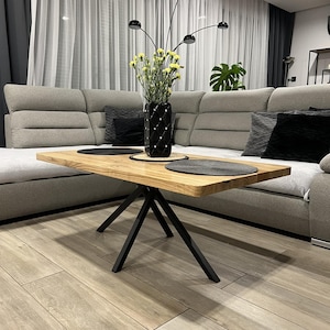 May include: A wooden coffee table with a black metal base. The table has a natural wood finish and a rectangular shape. The table is sitting on a light wood floor.