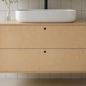 May include: A light wood floating bathroom vanity with two drawers and black circular pulls. A white, rectangular sink sits atop the vanity. The vanity is mounted on a tiled wall. A vase with greenery is on the left.