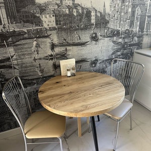 以下が含まれることがあります： 黒い脚とベージュのクッション付きの椅子が付いた丸い木製のテーブル。テーブルには塩とコショウの入れ物が置かれています。背景は白黒の都市の画像です。