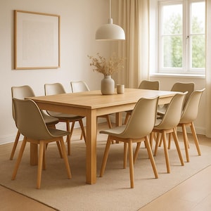 Op de afbeelding: Een lichte houten eettafel met acht beige stoelen. De stoelen hebben houten poten en gebogen rugleuningen. De tafel is rechthoekig. Een ingelijste foto hangt op de achtergrond aan de muur.