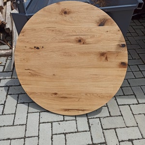 以下が含まれることがあります： 自然な木目仕上げの丸い木製テーブルトップ。テーブルトップは薄い茶色で、表面は滑らかです。木目は見やすく、木目にいくつかの節があります。