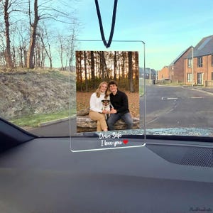May include: Transparent acrylic car ornament featuring a photograph of a couple and a dog. The ornament has the text "Drive Safe I love you" in white with a red heart. A black cord is attached for hanging.