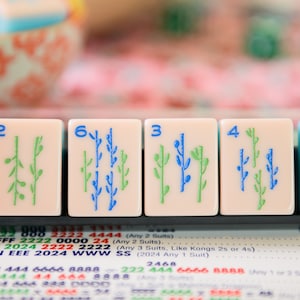 May include: Five mahjong tiles with green and blue bamboo designs. The tiles are numbered 2, 6, 3, 4, and 9. The tiles are on a black tray with a white background.