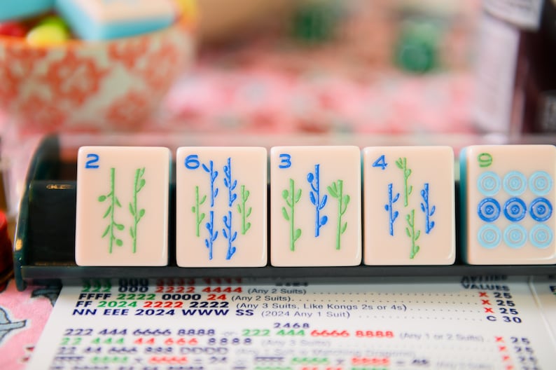 May include: Five mahjong tiles with green and blue bamboo designs. The tiles are numbered 2, 6, 3, 4, and 9. The tiles are on a black tray with a white background.