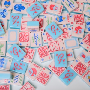 May include: A collection of colorful mahjong tiles with various symbols and numbers. The tiles are made of plastic and have a glossy finish. Some of the tiles feature a red "G" with a star.