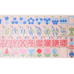 May include: A set of 36 mahjong tiles with various symbols and numbers. The tiles are pink with blue, green, and red accents. The tiles are arranged in four rows of nine tiles each. The tiles include numbers 1 through 9, bamboo, circles, characters, wind tiles, dragon tiles, and a joker tile.