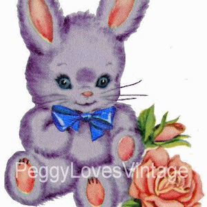 Pode incluir: Um coelho de pelúcia roxo com uma gravata borboleta azul segurando uma rosa rosa. O coelho tem orelhas cor-de-rosa e olhos azuis.