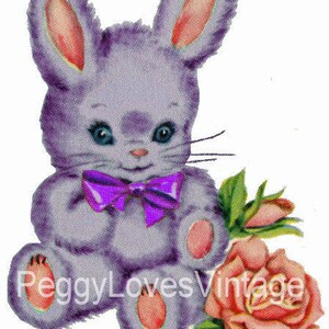 Pode incluir: Um coelho de pelúcia roxo com um laço roxo está sentado segurando uma rosa rosa. O coelho tem orelhas rosas e um nariz branco. A rosa tem folhas verdes.