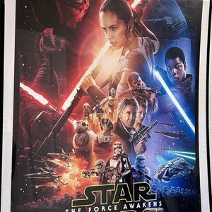 May include: A framed movie poster for Star Wars: The Force Awakens. The poster features characters with lightsabers, spaceships, and the film's title. Dominant colors include red, blue, and black.