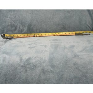 May include: A vintage walking stick with a curved handle and a metal tip. The stick is made of wood and has a decorative pattern. A yellow measuring tape is placed along the stick, showing measurements up to 25 inches.