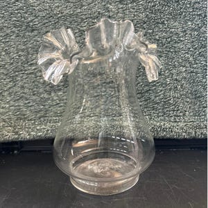 May include: A clear glass vase with a ruffled rim. The vase has a bulbous body and a flared base. The ruffled rim adds a decorative touch to the vase. The vase is made of clear glass.
