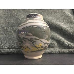 May include: A ceramic vase with a round body and a narrow neck. The vase features a marbled design in shades of gray, white, green, and yellow. The base and rim are a creamy white color. The vase is a decorative item.