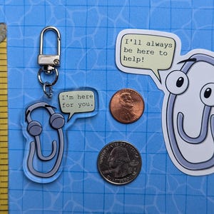 May include: Two paperclip-shaped keychains with different sayings. One keychain is a blue paperclip with the text "I'm here for you." The other keychain is a white paperclip with the text "I'll always be here to help!"
