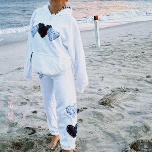 May include: A white hoodie with a black and blue heart design. The hoodie is paired with white sweatpants that also have a black and blue heart design.
