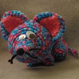 May include: A crocheted mouse toy with pink ears, blue and pink yarn, and a black button eye.