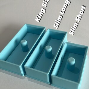 Könnte beinhalten: Drei blaue Kunststoffschalen in verschiedenen Größen, beschriftet mit "King Size", "Slim Long" und "Slim Short".