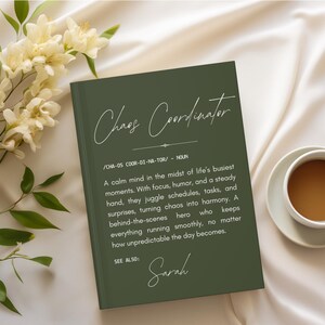May include: A green notebook with the words "Chaos Coordinator" in elegant script. The definition of the term is printed below, along with the name "Sarah". A cup of coffee and flowers are in the background.