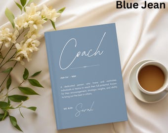 May include: A blue journal with the word "Coach" in white script. The journal includes a definition of "Coach" and the name "Sarah". A cup of coffee sits on a saucer to the right of the journal.