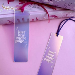 May include: Two iridescent bookmarks with a gradient of purple and blue. The bookmarks are rectangular and have the text "just one more page..." printed in white.