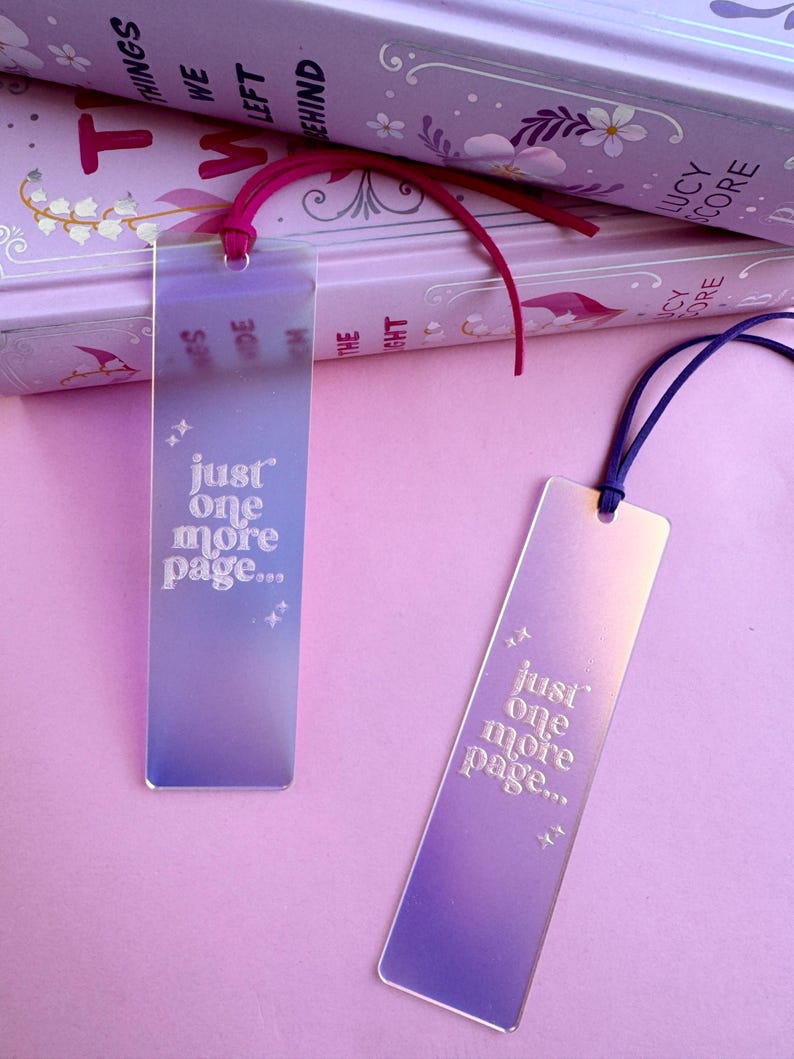May include: Two iridescent bookmarks with a gradient of purple and blue. The bookmarks are rectangular and have the text "just one more page..." printed in white.