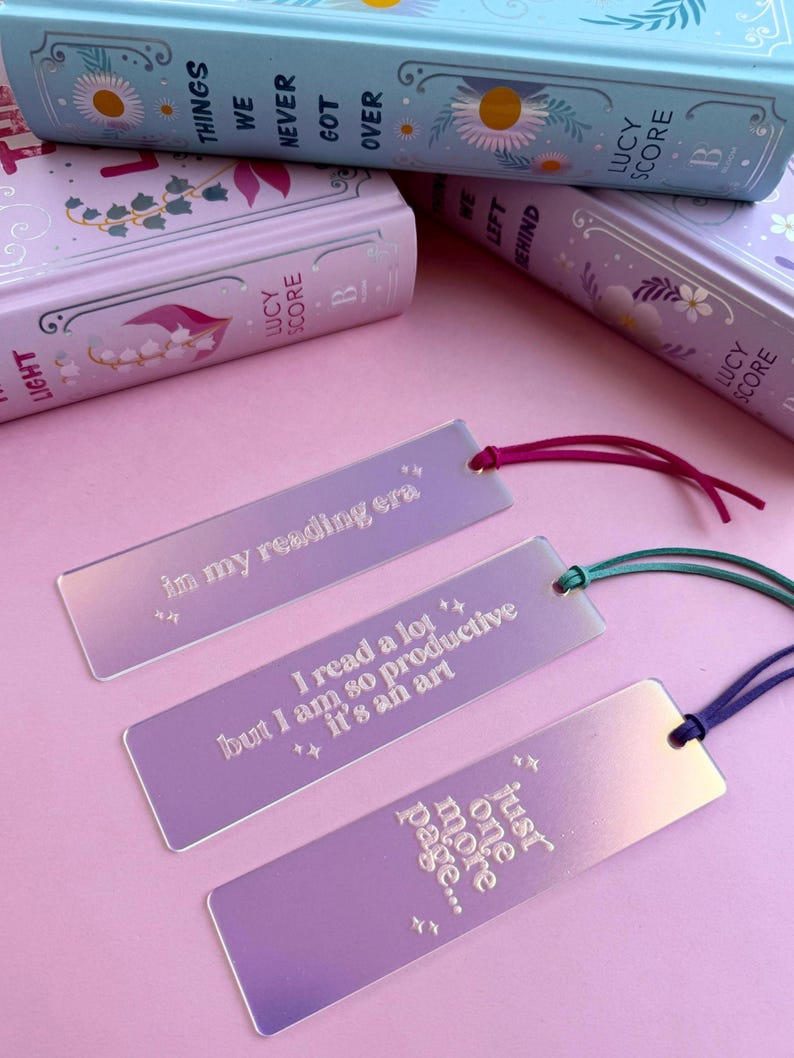 May include: Three iridescent bookmarks with pink, purple, and blue hues. The bookmarks feature quotes about reading: "in my reading era", "I read a lot but I am so productive it's an art", and "just one more page...".
