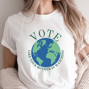 May include: White t-shirt with a green and blue graphic of the Earth and the text "VOTE LIKE YOUR MOTHER IS WATCHING".