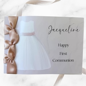 May include: A First Communion card with a watercolor illustration of a white dress with a pink sash. The card is decorated with a satin ribbon and the text reads "Jacqueline, Happy First Communion."