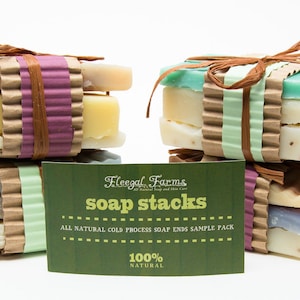 May include: Two stacks of natural soap bars wrapped in brown paper with twine. The soap bars are arranged in a variety of colors and textures. The stacks are labeled "Fleegal Farms soap stacks" and "All Natural Cold Process Soap Ends Sample Pack 100% Natural".