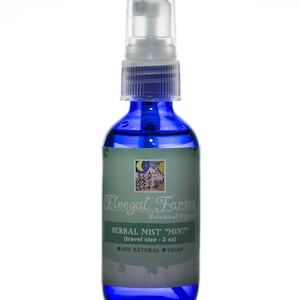 May include: A blue glass spray bottle containing herbal mist. The label reads "HERBAL MIST 'MINT'" and "(travel size - 2 oz)". The bottle has a clear plastic spray top and is labeled "100% NATURAL VEGAN".