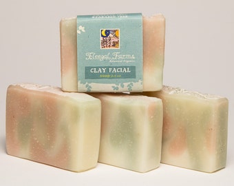 May include: Five bars of clay facial soap are stacked. The soap has a light green, pink, and white swirl pattern. A light blue label on one bar reads "Fleeal Farms Botanical Organics Clay Facial Soap (4.5 oz)" with a small illustration.