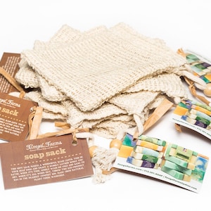 May include: A stack of natural beige soap sacks made from plant fibre. The sacks are tied with brown twine and have a wooden bead at the end. The image includes two brown cards with the text "Royal Farms Soap Sack" and a white card with the text "RoyalFarms.com | 512.397.SOAP | RoyalFarmsNaturallySoaps.com".