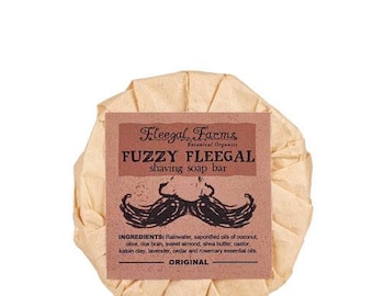 May include: A brown paper-wrapped bar of shaving soap with a label that reads "Fleegal Farms Botanical Organics Fuzzy Fleegal shaving soap bar" and lists the ingredients: Rainwater, saponified oils of coconut, olive, rice bran, sweet almond, shea butter, castor, kaloin clay, lavender, cedar and rosemary essential oils. The label also says "ORIGINAL".