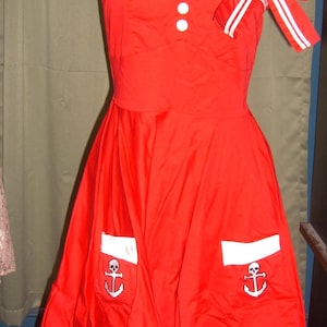 May include: A red halter dress with white trim and a bow. The dress features white buttons, pockets with skull and anchor designs, and the text "SINCE 150".