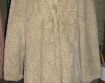 Peut inclure: Manteau en fausse fourrure crème avec un grand col et trois boutons. Le manteau est présenté sur un mannequin rouge. Le tissu a un motif texturé et bouclé, et le manteau semble arriver au genou.